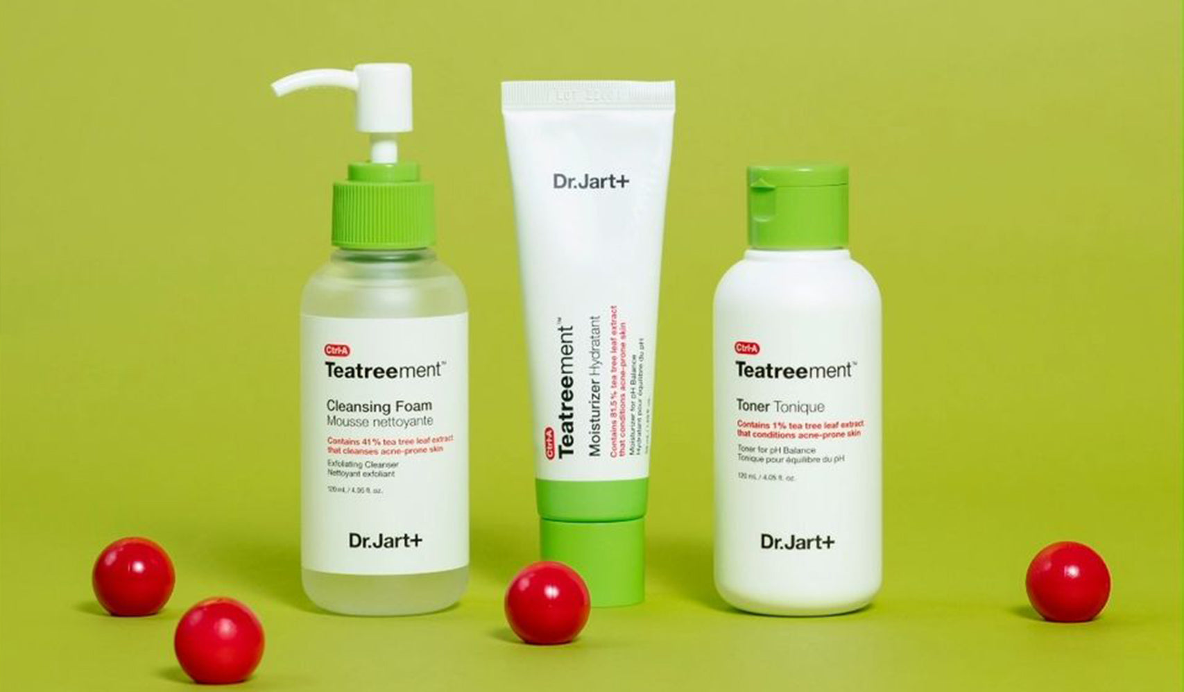 Dr.Jart+ Teatreement skincare set with cleansing foam, toner, and moisturizer displayed on a green background with red spheres.