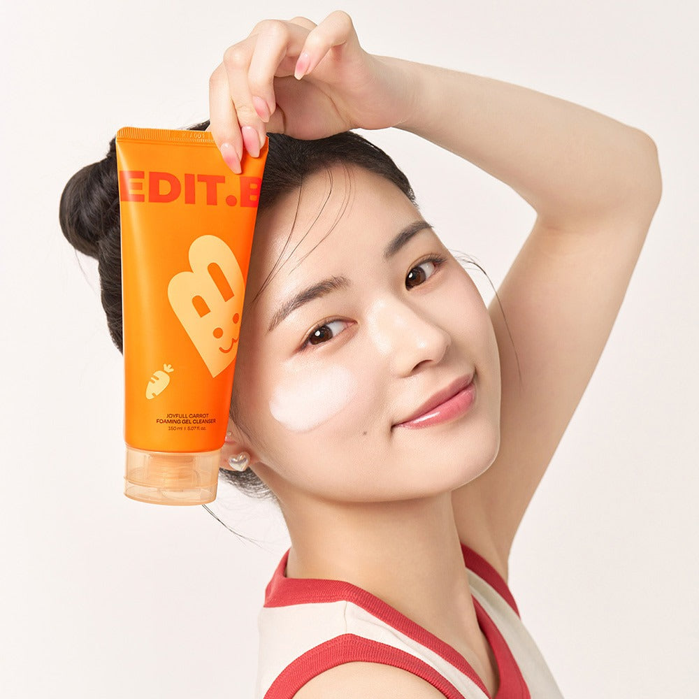 Woman holding EDIT.B Joyful Carrot Foaming Gel Cleanser 150ml next to her face, showcasing skincare application