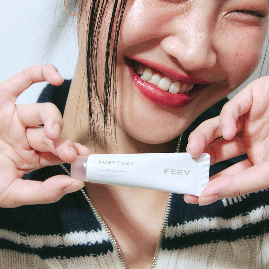 Smiling individual holding FEEV Hyper-Fit Color Balm in a close-up shot.