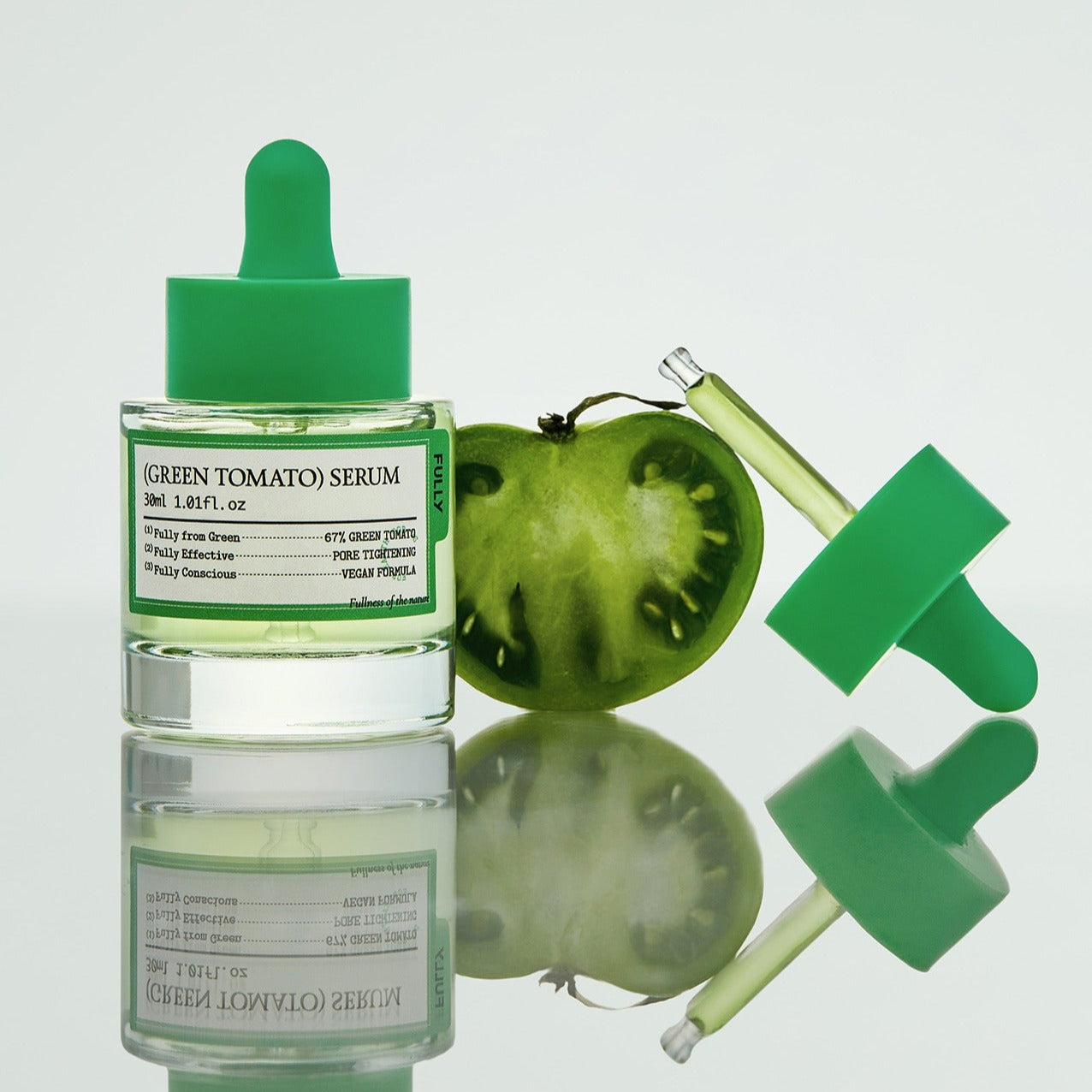 FULLY Green Tomato Serum 30ml with a sliced green tomato and dropper on a reflective surface showcasing skincare serum.