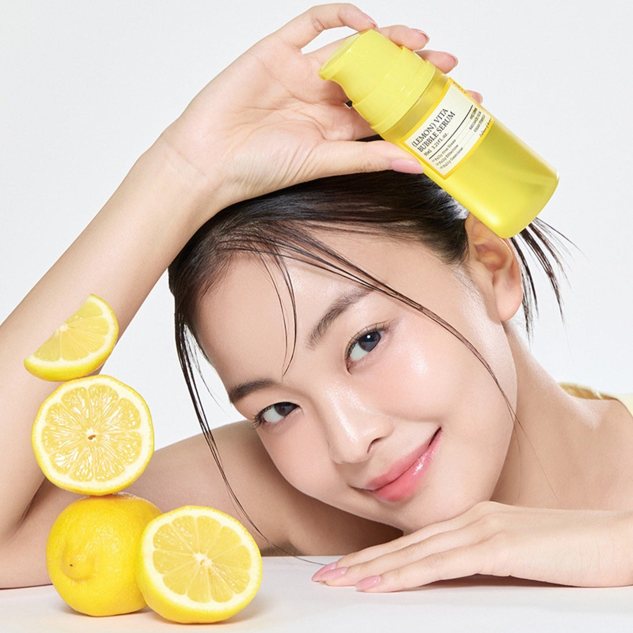 Smiling woman holding FULLY Lemon Vita Bubble Serum 95ml bottle, surrounded by fresh lemons, showcasing skincare benefits.