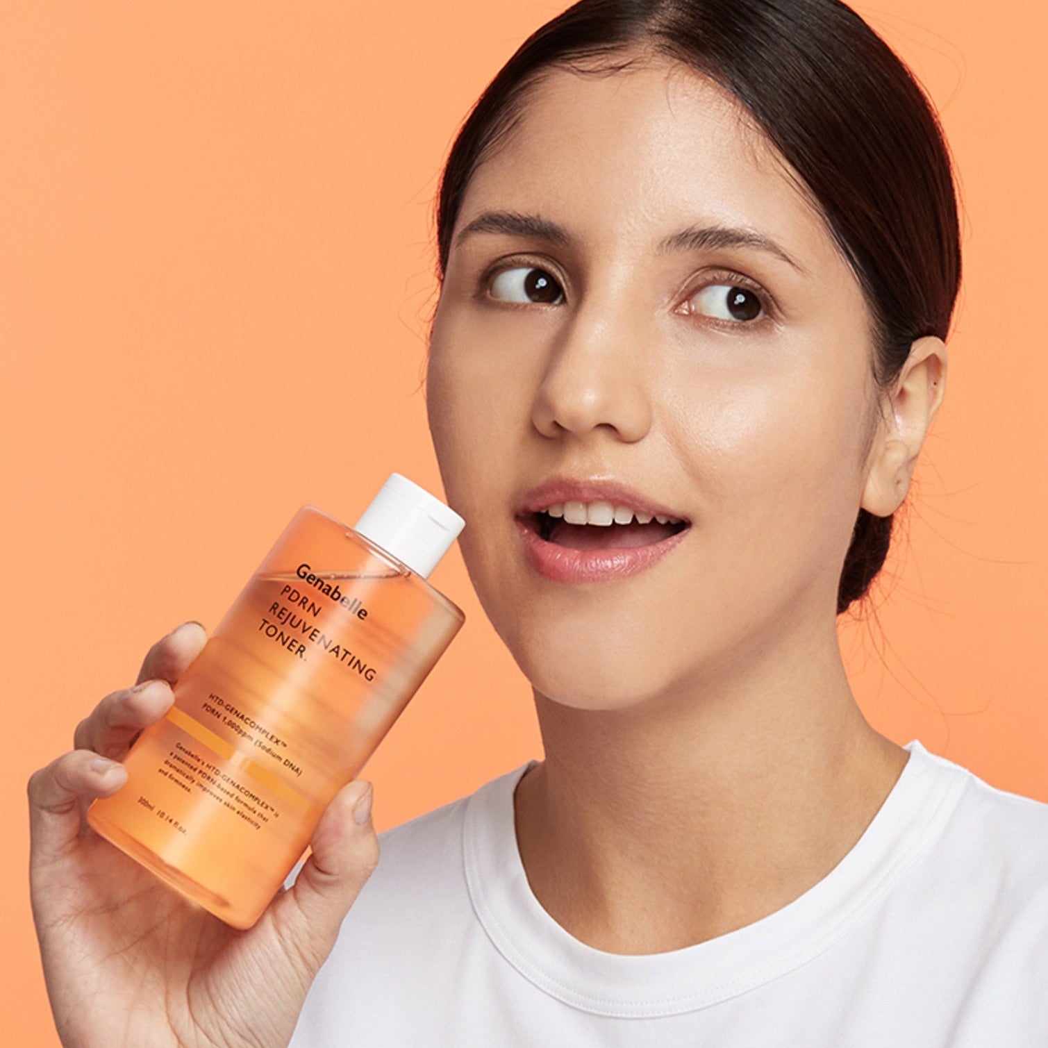 Woman holding GENABELLE PDRN Rejuvenating Toner 300ml against an orange background.