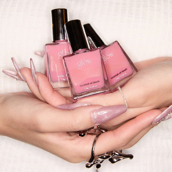 Three bottles of GLOW Cocktail Oil Blusher 7.5g in a person's hands with elegant nail art.