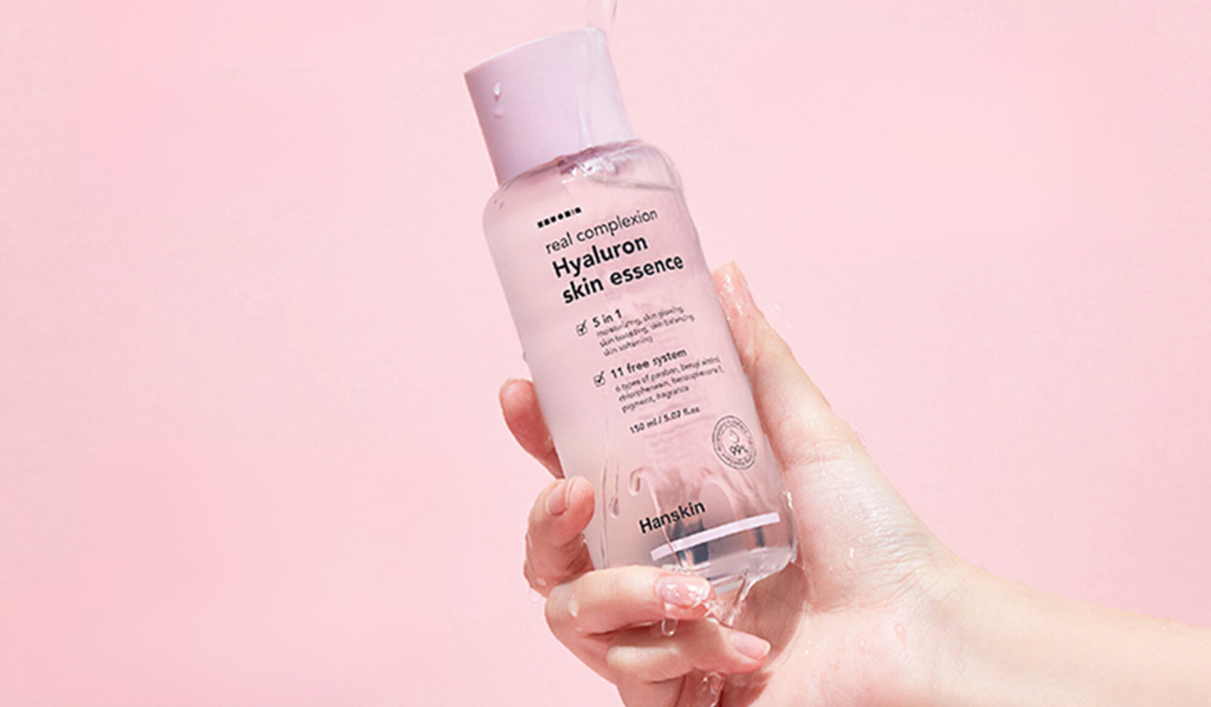 Hand holding a bottle of hyaluron skin essence against a pink background