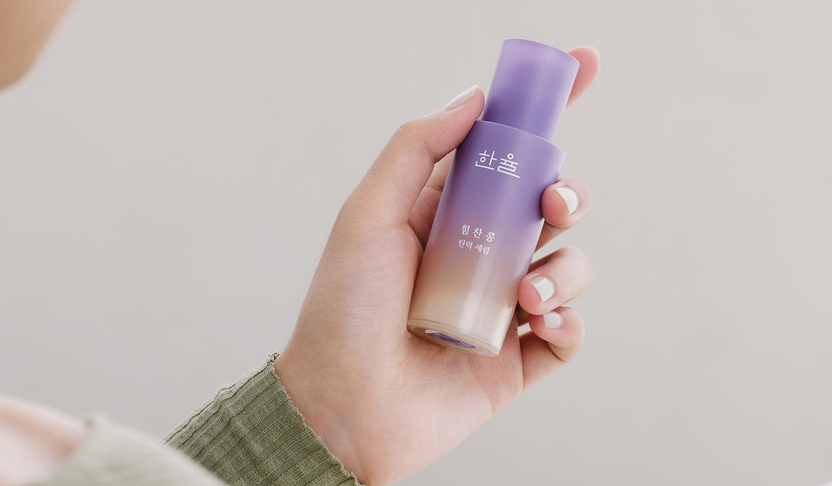 Hand holding a purple skincare bottle against a neutral background