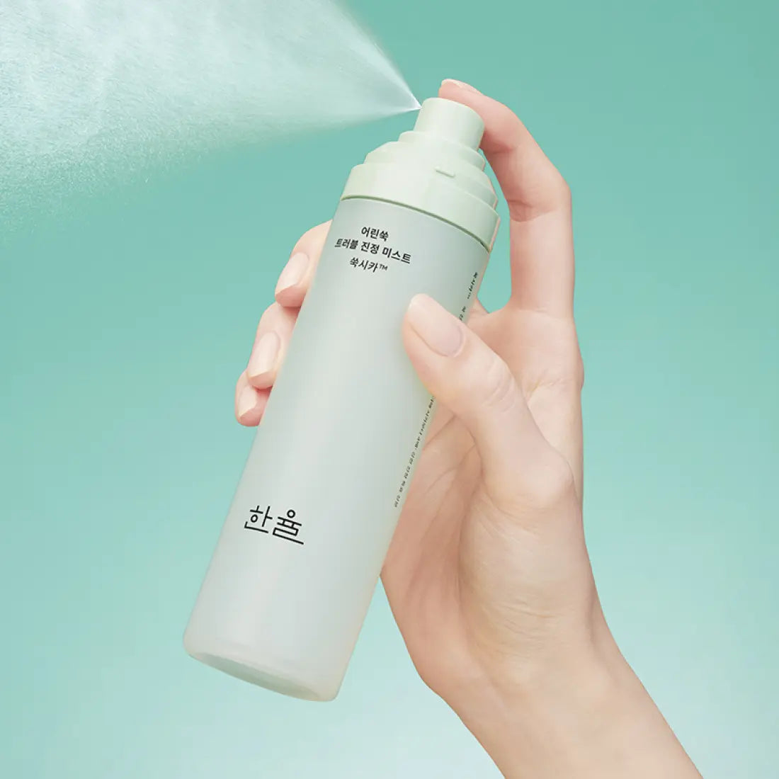 Hand holding HANYUL Young Artemisia Trouble Mist 120ml against a green background