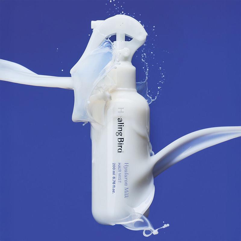 HEALING BIRD Hyalutonic Milk Hair Mist 200ml beauty product in white bottle with splashing milk on blue background.