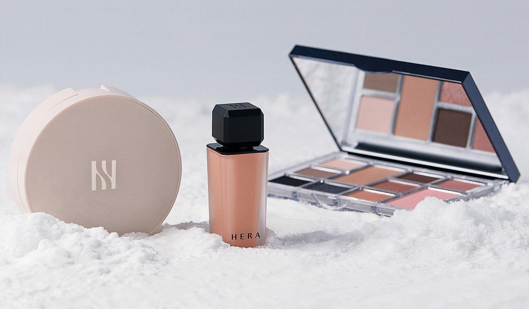 Luxury makeup set with foundation, compact powder, and eyeshadow palette displayed on a snowy surface.