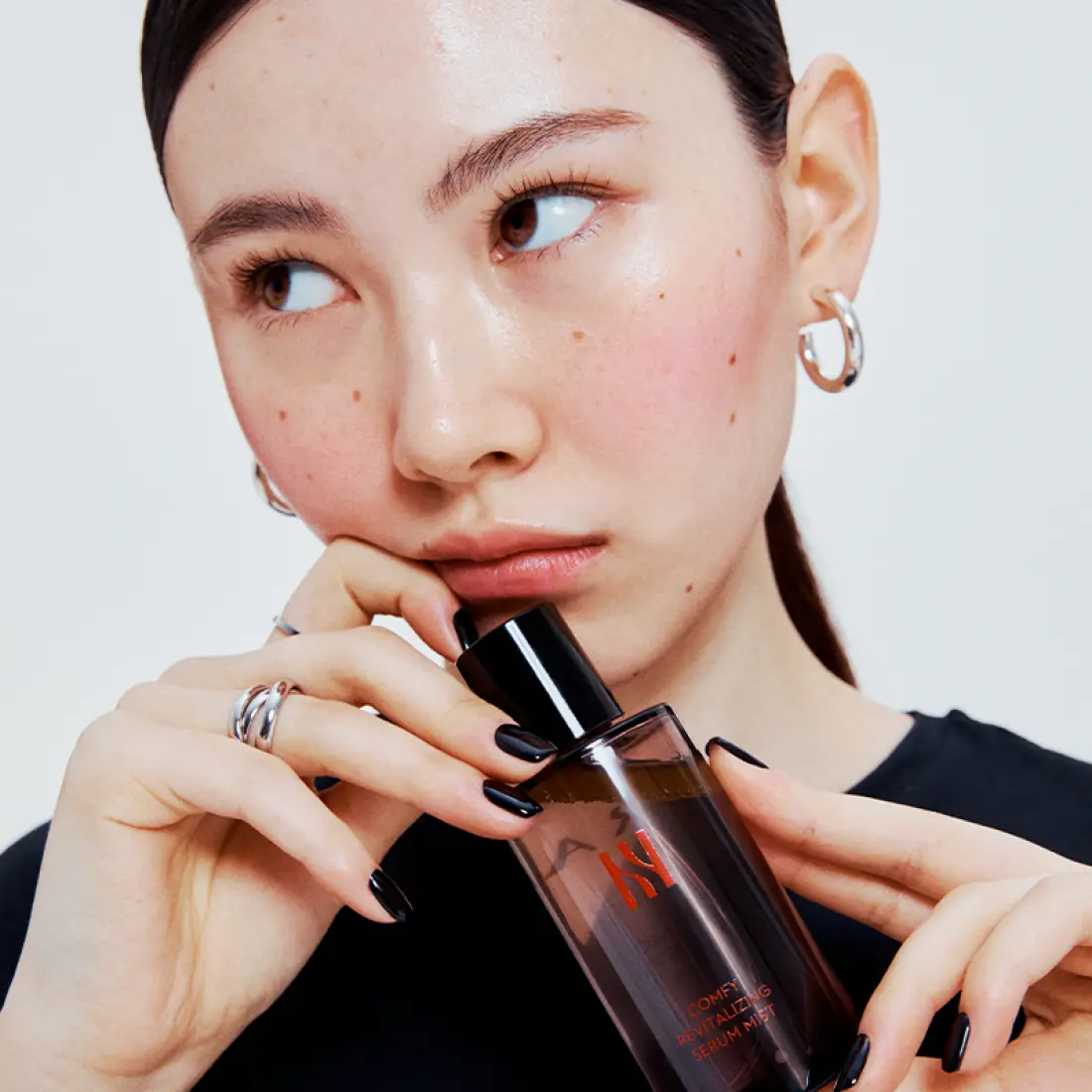 Woman holding HERA Comfy Revitalizing Serum Mist 90ml bottle, showcasing skincare product for healthy complexion.