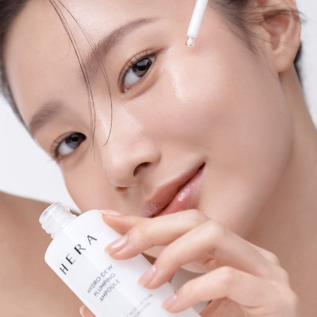 Woman applying HERA Hydro-Dew Plumping Ampoule 50ml on face for hydration and skincare.
