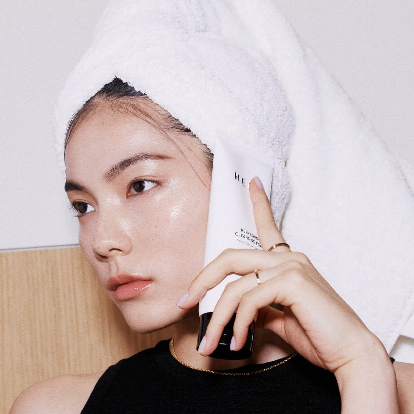 Person holding HERA Refreshing Cleansing Foam 160g next to face, showcasing skincare product.