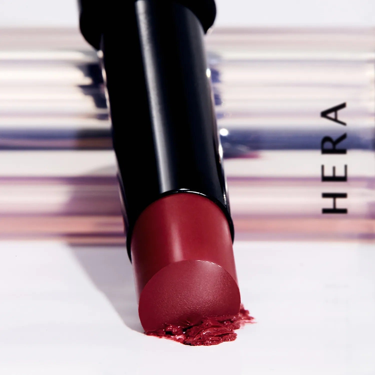 HERA Sensual Tinted Shine Stick 3.5g lipstick close-up with smudged tip against elegant background for beauty products.