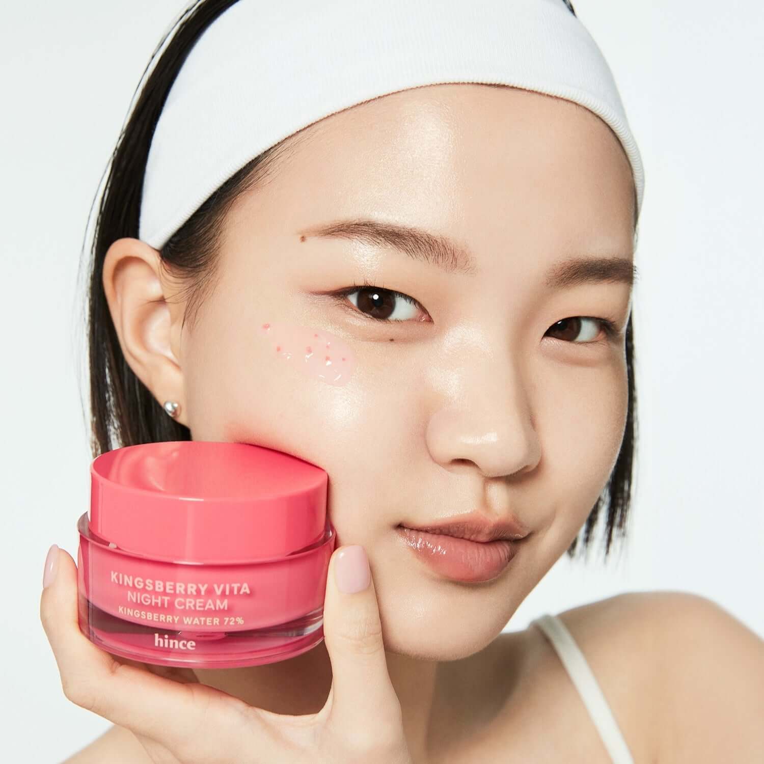 Woman holding HINCE Kingsberry Vita Night Cream jar near her face with a gentle smile.