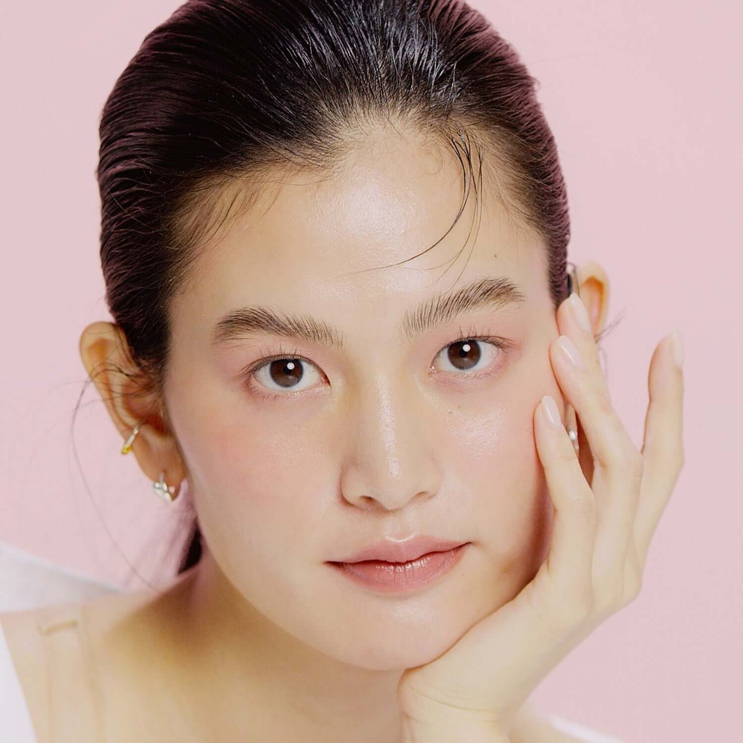 Model with smooth skin using HINCE Second Skin Hydrating Primer against a pink background, showcasing the product's moisturizing effect.