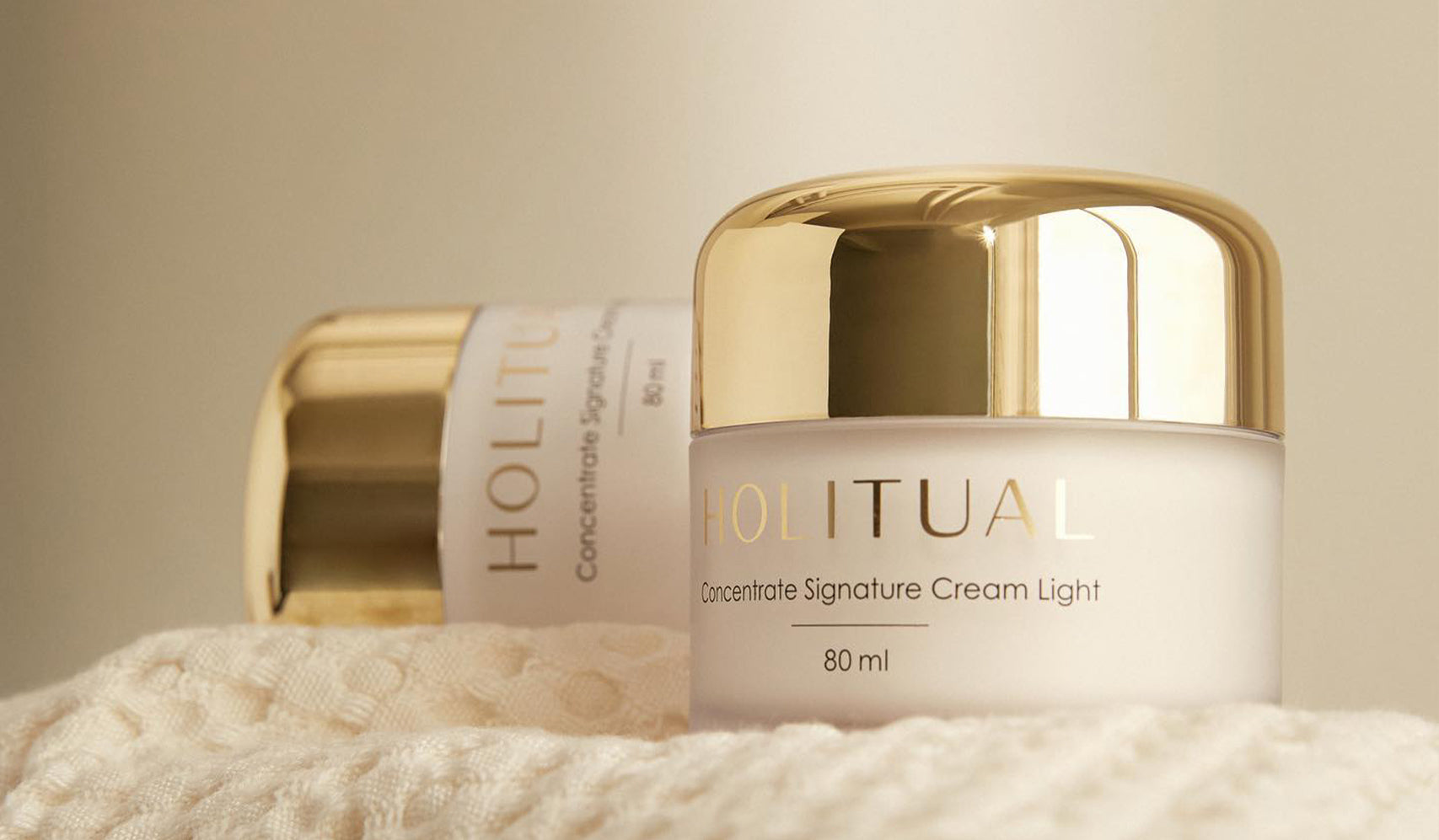 Luxurious Holitual skincare cream jars with gold lids on a soft textured cloth