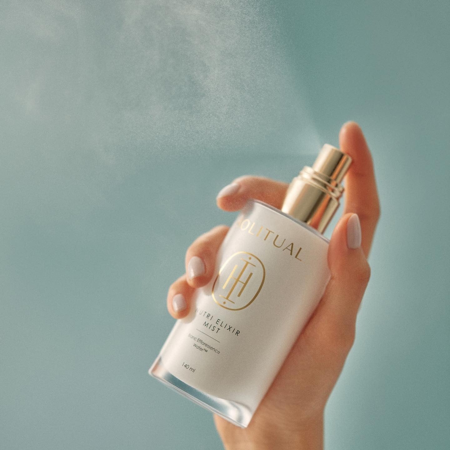 Hand holding a bottle of HOLITUAL Elixir Mist 140ml against a blue background
