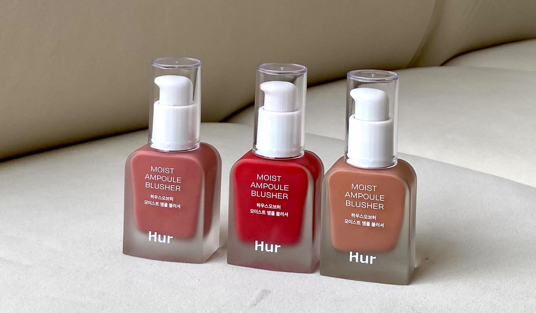 Three bottles of Hur moist ampoule blusher in different shades, displayed on a beige background.