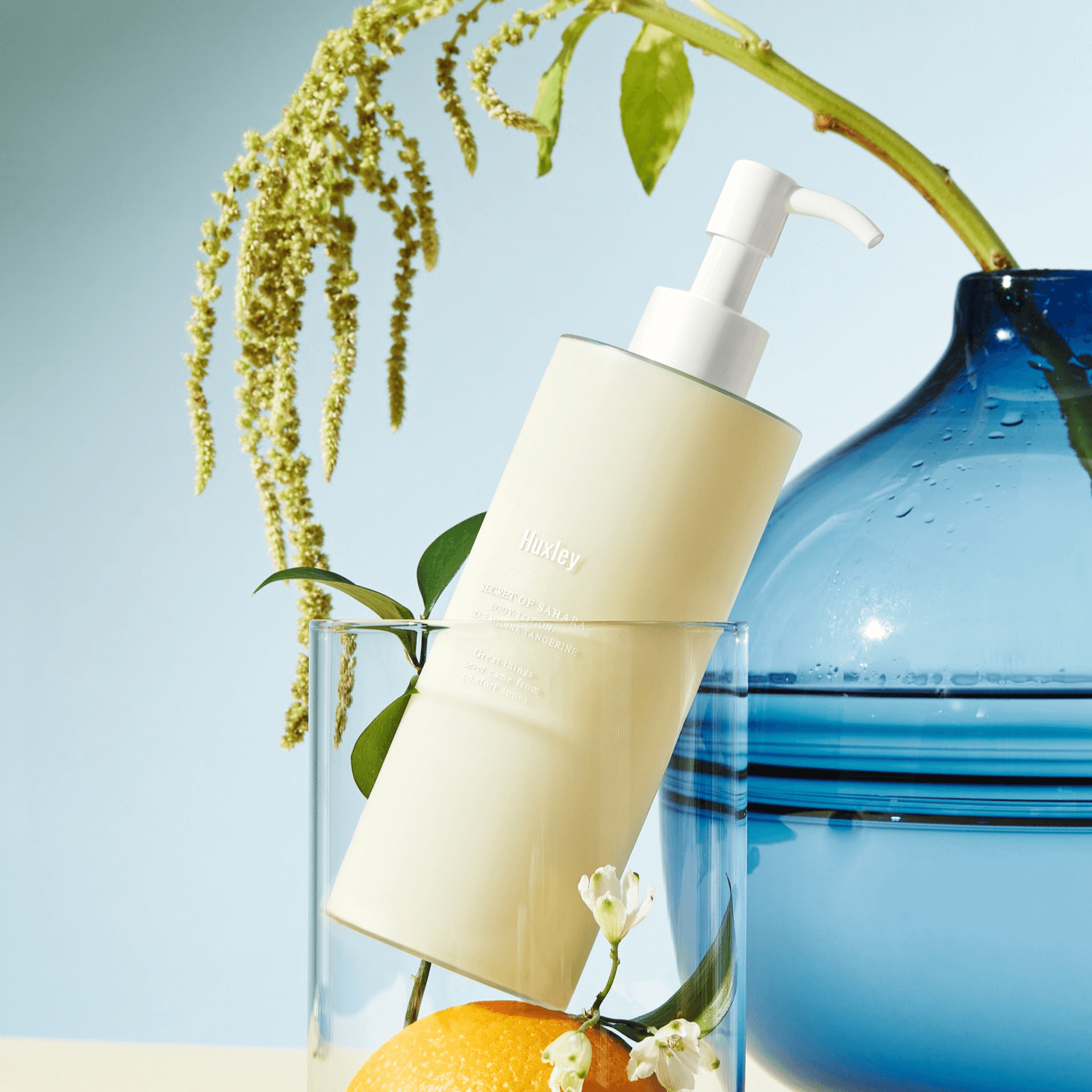 HUXLEY Body Lotion Blue Madina Tangerine bottle with pump on display with decorative elements in the background