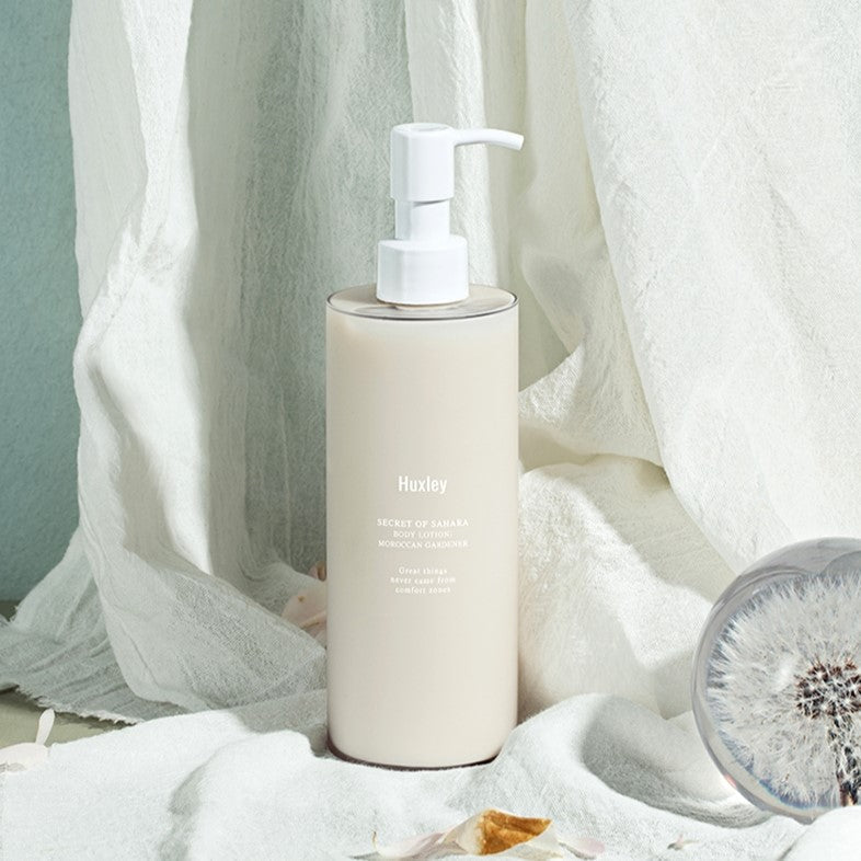 HUXLEY Body Lotion Moroccan Gardener 300ml bottle on fabric with dandelion glass orb, highlighting luxurious skincare product.
