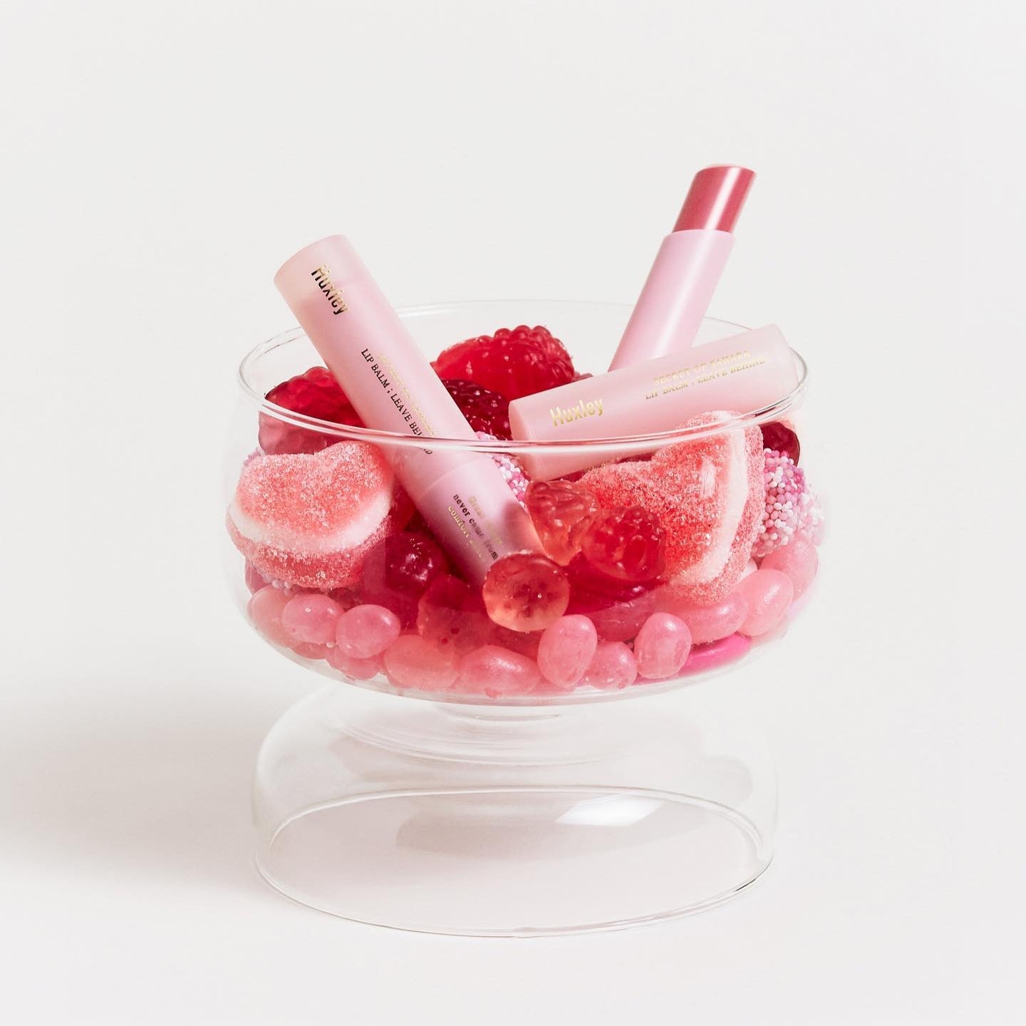 HUXLEY Lip Balm Leave Behide in glass bowl with pink decorative candies
