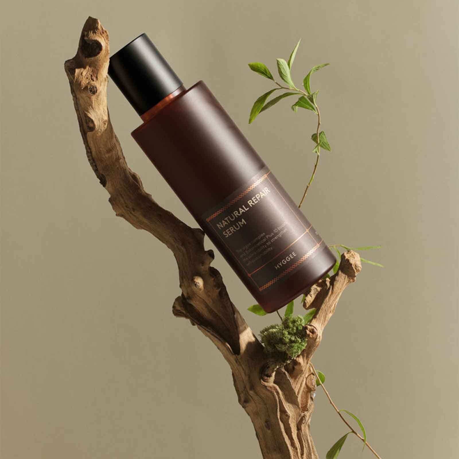 HYGGEE Natural Repair Serum 120ml bottle displayed on a natural wood and plant setting, highlighting organic skincare essence.