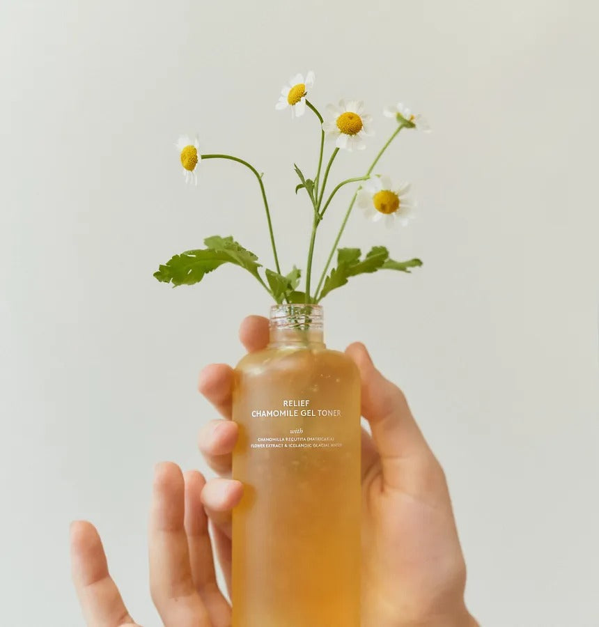 HYGGEE Relief Chamomile Gel Toner 200ml in a clear glass bottle with chamomile flowers, held by a hand against a neutral background