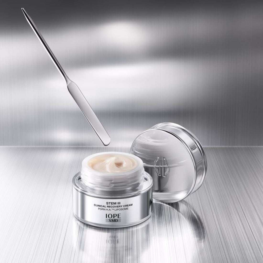 IOPE XMD Stem3 Clinical Recovery Cream 50ml with spatula on metallic background