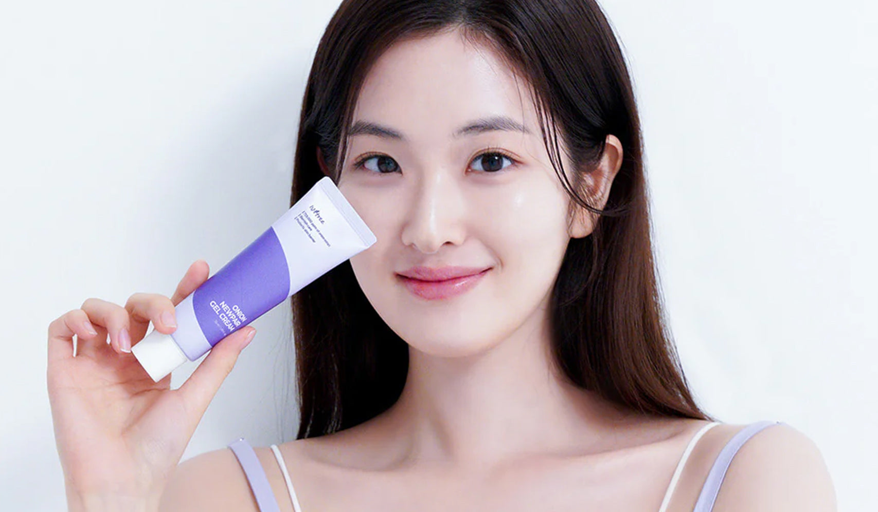 Woman holding cosmetic skin cream tube with purple label, smiling, skincare product demonstration
