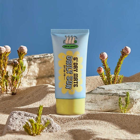IT'S SKIN Good Day Mate Daily Sun SPF50+ PA++++ sunscreen tube on sandy beach setting with plants and rocks.