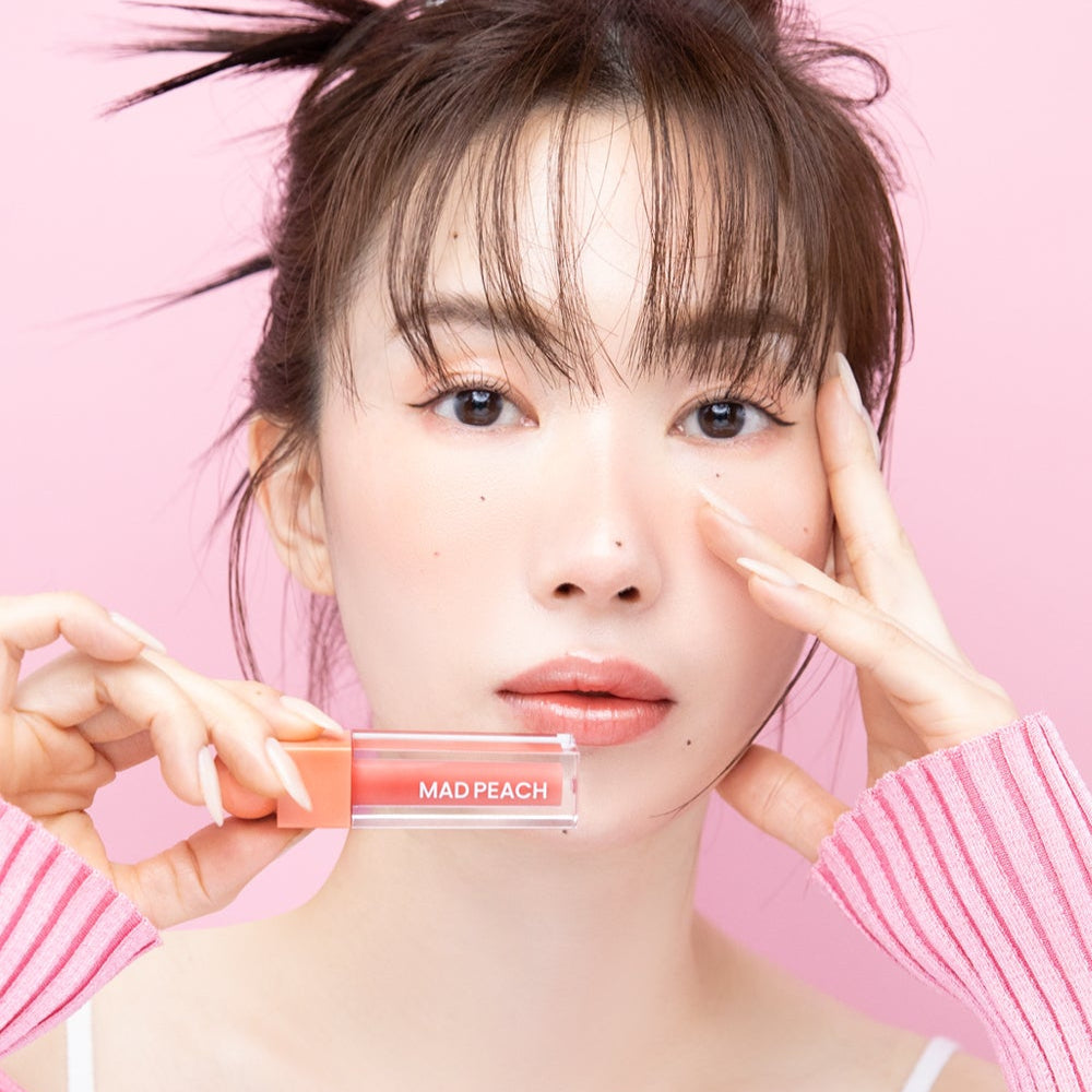 Woman holding IVI MAD PEACH Glow Fit Mood Gloss against pink background