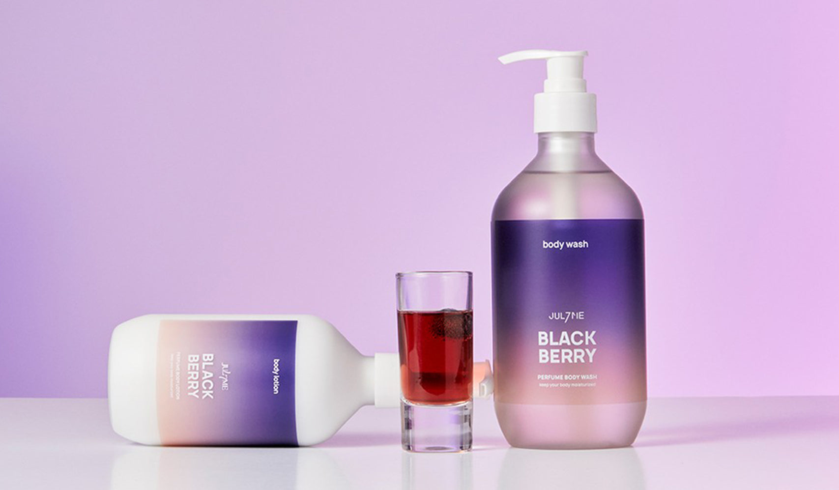 Blackberry-scented body wash bottles with a purple gradient background and a small glass filled with dark red liquid.