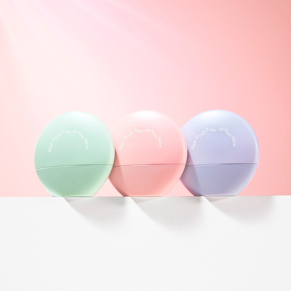 Collection of KAHI One Layer Tone-up Sun Skin 40ml in green, pink, and purple containers against a pink background.
