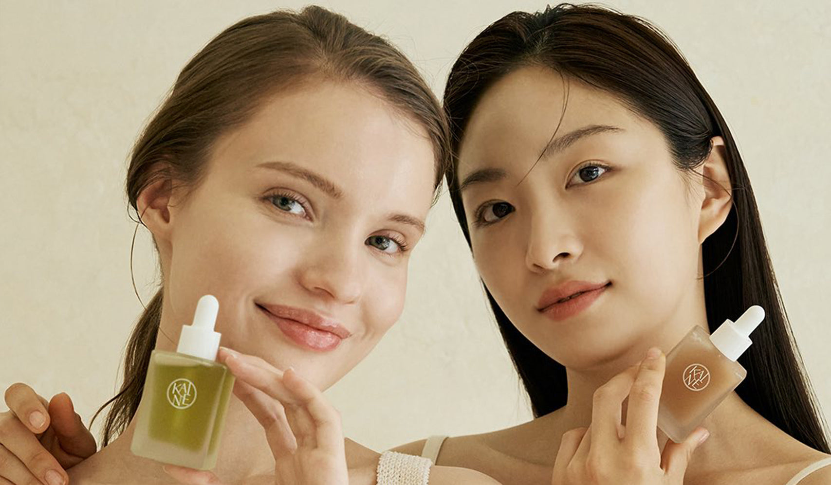 Two women holding skincare serum bottles, smiling with clean, natural looks
