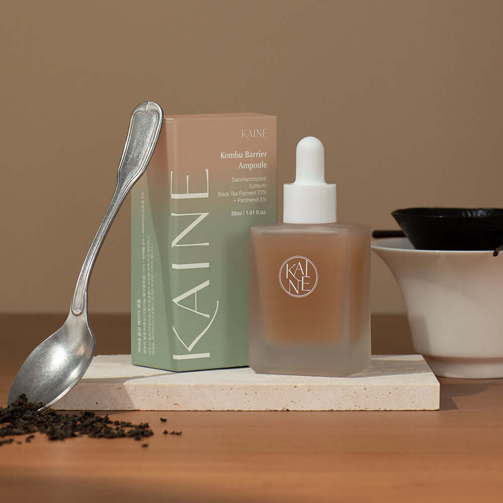 KAINE Kombu Barrier Ampoule with box on wooden table beside tea leaves and spoon