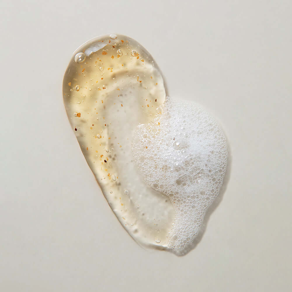 Texture of KAINE Kombu Hydrating Daily Cleanser 155g with foam and exfoliating particles on a light background.