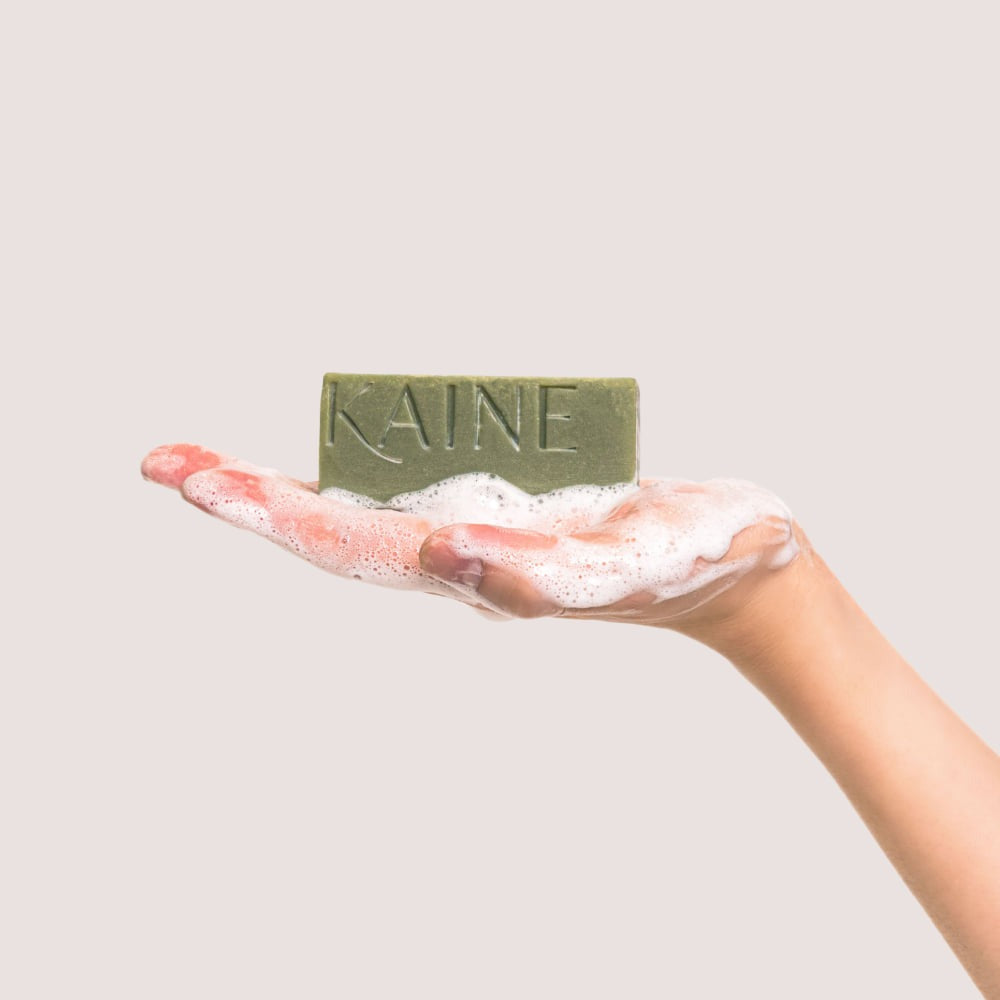 Hand holding KAINE Rosemary Acne Mildly Acidic Cleansing Bar 100g with soap suds
