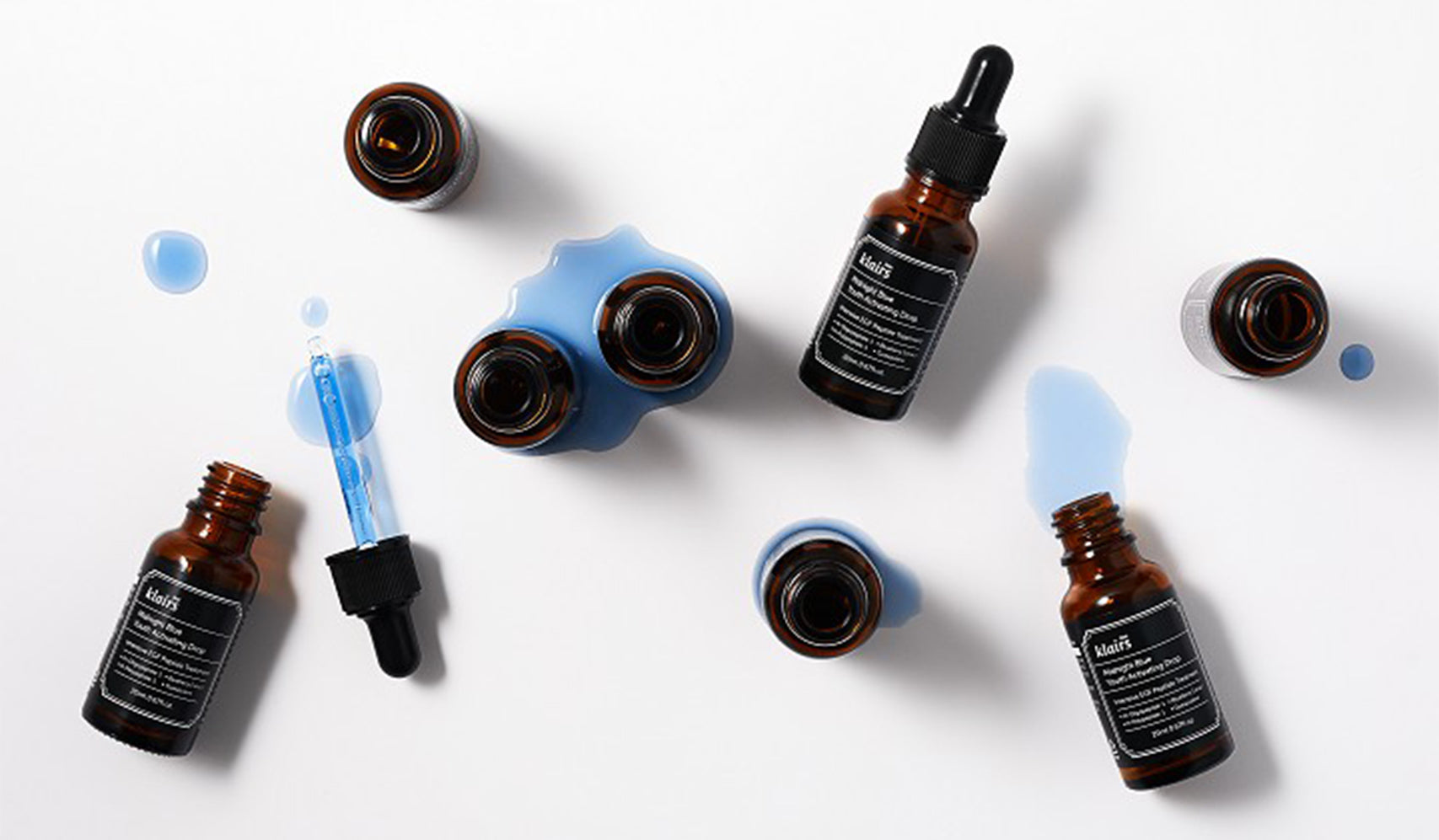 Brown glass dropper bottles and blue liquid on white background, flat lay of skincare products.
