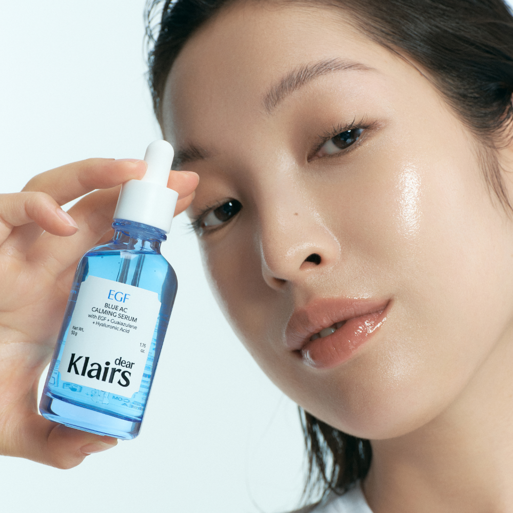 Woman holding KLAIRS EGF Blue AC Soothing Serum 50g bottle with glowing skin
