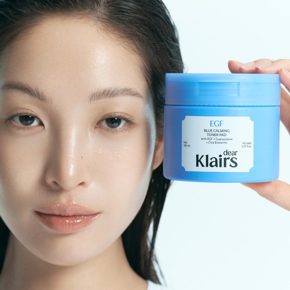 Woman holding KLAIRS EGF Blue Calming Toner Pads 60 Pads product jar, showcasing skincare benefits.