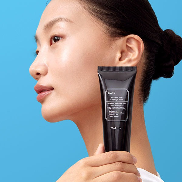 KLAIRS EGF Midnight Blue Calming Cream 60g held by a model with clear skin against a blue background