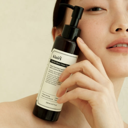 Woman holding KLAIRS Gentle Black Deep Cleansing Oil 150ml bottle to her face, showcasing skincare benefits.