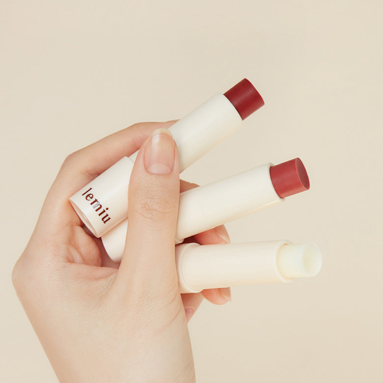 Hand holding three LEMIU Sole Mood Vegan Lip Balm tubes, showcasing red and clear balm options.