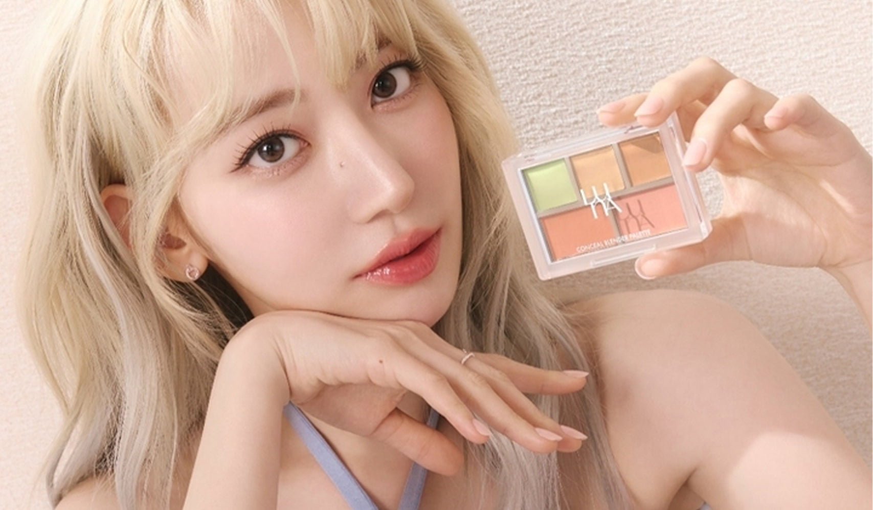 Woman showcasing colorful makeup palette against a light background, highlighting vibrant cosmetic choices for modern styling.