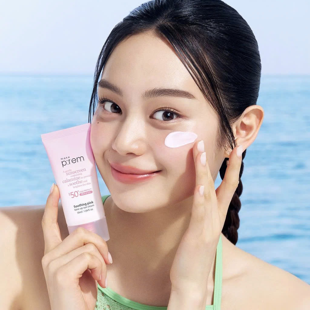 Woman applying MAKE P:REM Soothing Pink Tone-Up Sunscreen SPF 50+ PA++++ 50ml near ocean