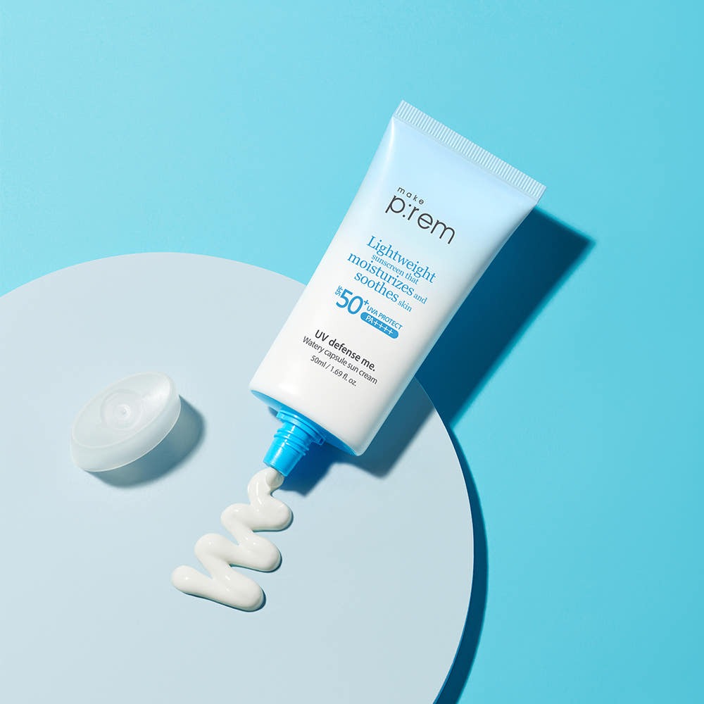 MAKE P:REM UV Defense Me Watery Capsule Sunscreen 50ml SPF50+ PA++++ displayed on blue surface, showcasing lightweight moisturizing formula.
