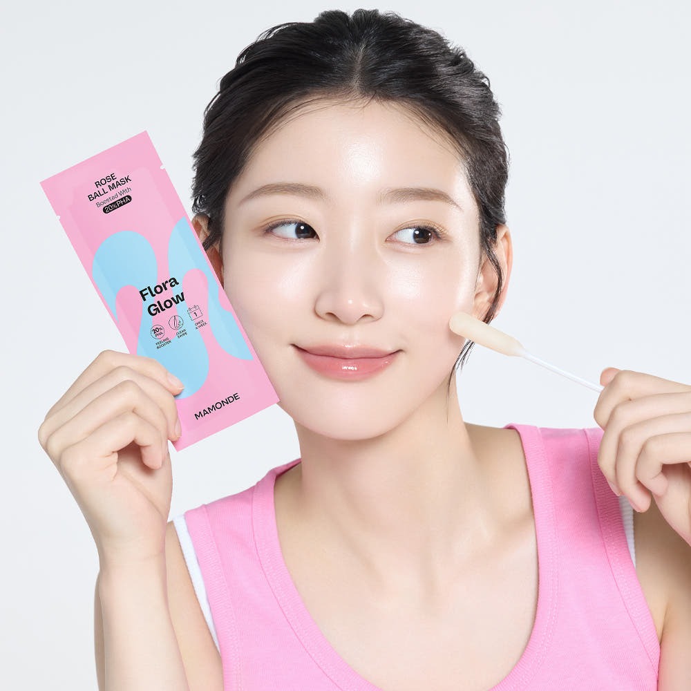Smiling woman applying MAMONDE Flora Glow Rose Ball Mask 3.5ml on face, holding mask sachet.