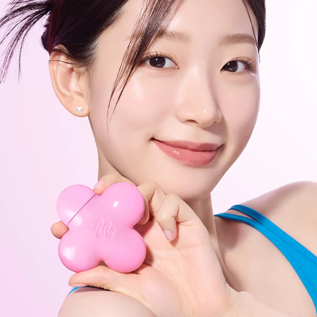 Person holding a pink flower-shaped beauty product case, smiling, with a clear complexion and wearing a blue top.