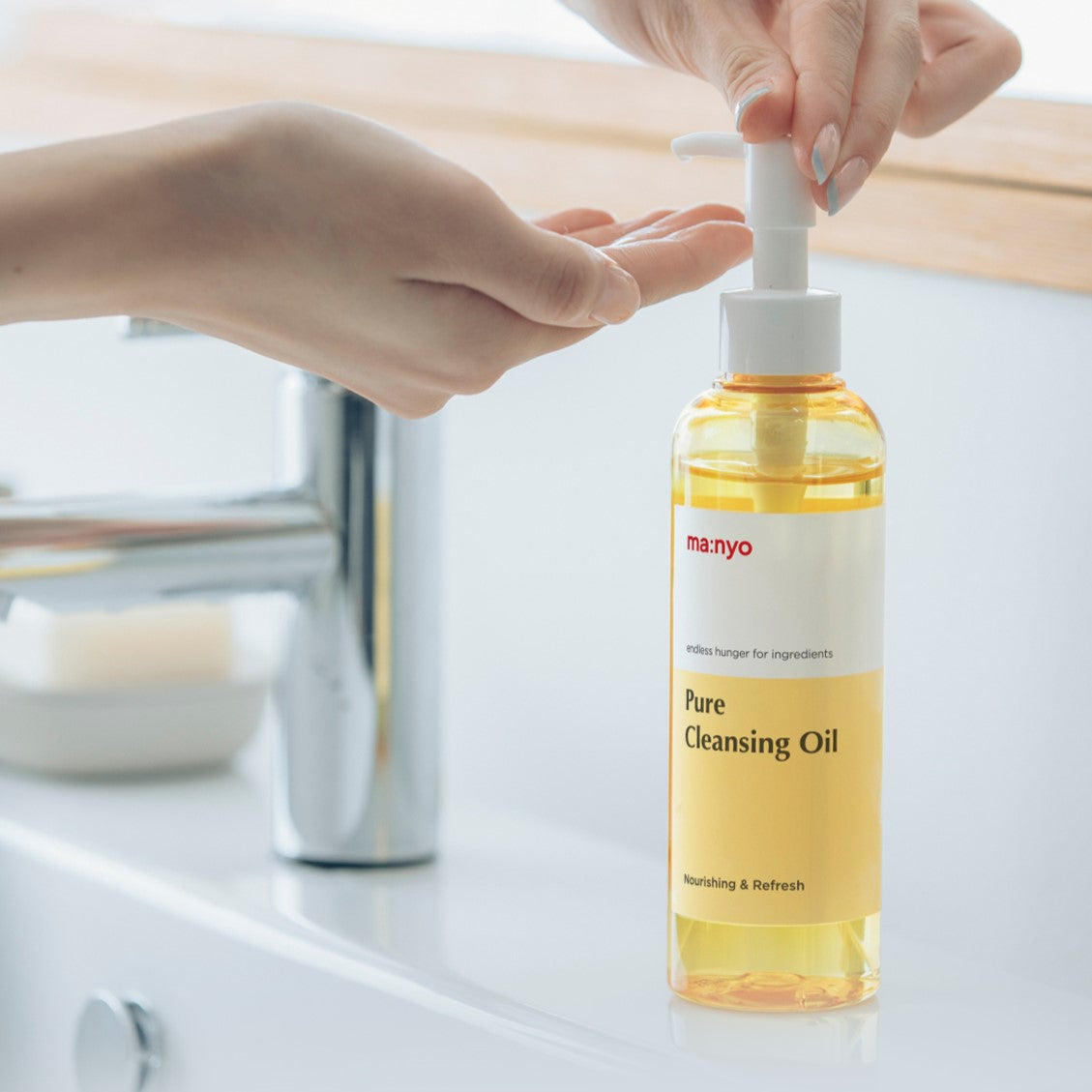 Person using MA:NYO Pure Cleansing Oil bottle at a sink, showcasing skincare product.