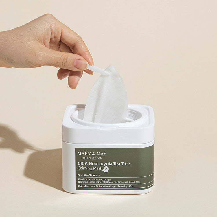 Hand holding a sheet mask from MARY & MAY Cica Houttuynia Tea Tree Calming Tree x30 container for soothing skincare.