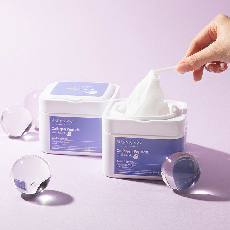 Hand holding tissue from MARY & MAY Collagen Peptide Vital Mask x30 container on a light purple background with glass spheres.